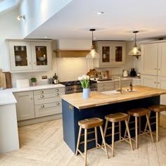 a kitchen with an island and stools in the center, surrounded by wooden flooring