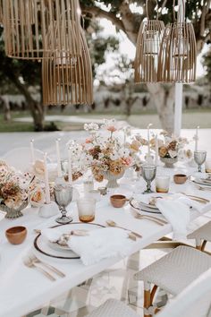 an outdoor table set up with white and gold plates, silverware and flowers in vases