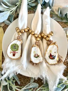 three white napkins with gold trim and embroidered designs on them sitting on a plate