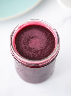 a glass filled with purple liquid sitting on top of a white countertop next to a plate