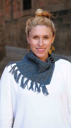 a woman with blonde hair wearing a white sweater and blue scarf smiles at the camera