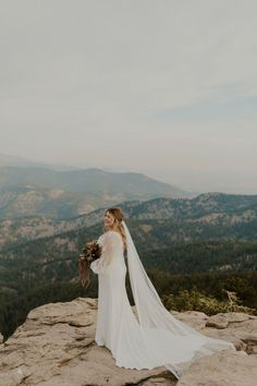 a woman in a wedding dress standing on top of a mountain