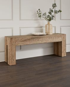 a wooden table with a vase on top of it next to a white wall and wood floor