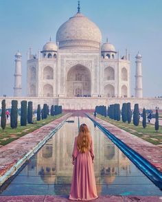 a woman standing in front of the tajwa mosque, with her reflection in the water