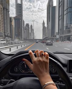 a person driving a car with their hand on the steering wheel and city buildings in the background