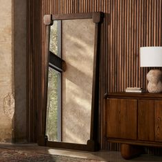 a large mirror sitting on top of a wooden dresser next to a wall mounted lamp