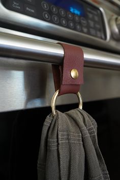 a close up of a cloth hanging from a hook on an oven door handle with a clock in the background