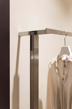 a white shirt is hanging on a metal pole in front of a wall mounted coat rack