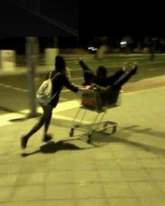 two people pushing a shopping cart down the street