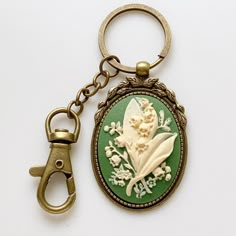 "Lily of the Valley Keychain Cameo Key Chain Floral Accessories -I make these keychains using your choice of Antique Silver or Antique Brass hardware, keychain hook along with a large clasp for clipping onto purses or adding other keychain accessories to; rose cameo is green and cream -Nickel free and lead free alloy metal, resin cameo -Select your finish from the dropdown menu -Measures 3\" long (from top of round keyring to bottom of cameo) x 1 3/8\" wide (cameo width) -Gift Boxed More of my L Antique Keychain, Lily Of The Valley Keychain, Vintage Keychains, Green Keychain, Vintage Keychain, Keychain Hook, Bridesmaid Favors, Clay Inspo, Antique Keys