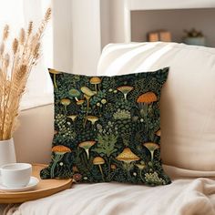 a pillow with mushrooms on it sitting on a couch next to a cup and saucer