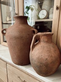 three clay vases sitting on top of a counter next to a clock and cabinet