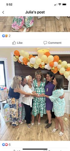 two women are shaking hands in front of balloons on the wall and another woman is standing behind them