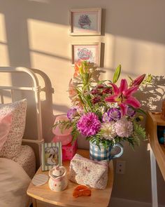 a vase filled with flowers sitting on top of a wooden table next to a bed