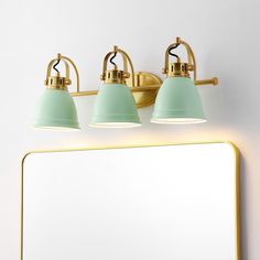 three light bathroom fixture with green shades in front of a white wall and gold framed mirror