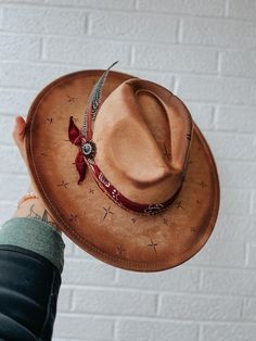 This wide brim fedora is a tan suede hat with hand burned crosses around the hat and an edge burn.  It is with a bandana, feathers, and rhinestone brooch. Edgy Cowgirl, Cowgirl Concert, Suede Hat, Hand Burn, Wide Brim Fedora, Rhinestone Brooches, Tan Suede, Fedora Hat, Wide Brimmed