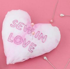 a heart - shaped pillow with the words sewn love on it and pins attached to it