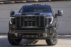 the front end of a black truck parked in a parking lot next to a building