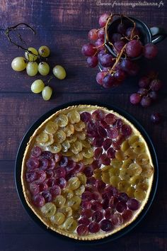 a pie with grapes and other fruit sitting on a wooden table next to a bowl of grapes