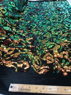 sequins on black fabric with gold and green details next to ruler for measuring