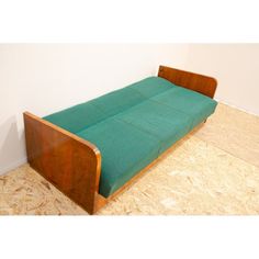 a green couch sitting on top of a hard wood floor next to a white wall