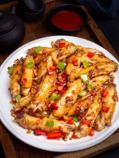 a white plate topped with chicken wings covered in sauce and green peppers on top of a wooden cutting board