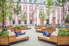 people sitting on wooden benches in the middle of a courtyard with many trees and plants