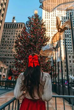 a woman standing in front of a christmas tree with a red bow on her head