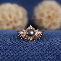 a black pearl and diamond ring sitting on top of a blue cloth