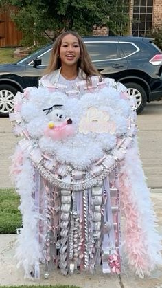 a woman standing in front of a car holding a large white teddy bear decoration on it's chest