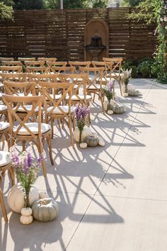 rows of wooden chairs with white cushions and flowers in vases sitting on the ground