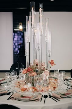 an elegant table setting with candles and flowers in vases on the centerpiece is surrounded by clear glassware