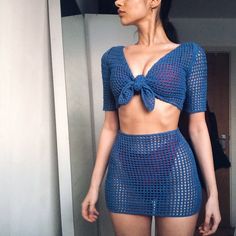 a woman wearing a blue crochet top and short shorts with a bow at the waist