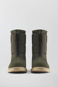 the back view of a pair of olive green boots with tan soles and rubber outs