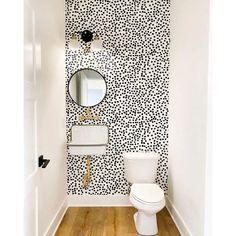 a white toilet sitting in a bathroom next to a wall with black dots on it