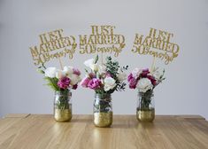 three vases with flowers in them sitting on a table next to a sign that says just married