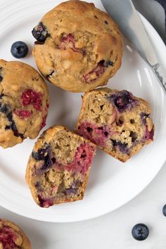 four blueberry muffins on a white plate next to a knife and fork