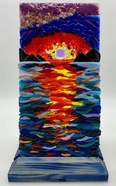 Presenting a Handmade Glass Fused Sunset - a 12x6 masterpiece in impressionist style, capturing the brilliance of a sunset reflecting on the ocean.  Enjoy breathtaking hues of a radiant sunset as depicted in this unique glass fusion artwork. The brilliant colors, meticulously fused together, capture the essence of the impressionist style, creating a harmonious blend of warm tones that dance across the glass canvas. The use of this technique lends a sense of fluidity and movement to the scene, truly bringing the sunset to life. What sets this piece apart is its ability to illuminate from behind, casting a mesmerizing glow that enhances the overall ambiance of any room. Place it near a light source, and watch as the vibrant colors come alive, creating a captivating play of light and shadow. Fused Glass Sunset, Art Sunset, On The Ocean, Glass Fusion, Fused Glass Art, Glass Art Sculpture, Glass Sculpture, The Sunset, Brilliant Colors