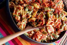 a bowl filled with pasta and sauce on top of a table next to a wooden spoon