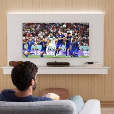 a man sitting on a couch in front of a flat screen tv with the soccer game on it