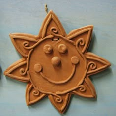 a clay sun face hanging from a hook on a blue wall with other items in the background