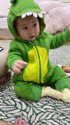 a baby in a green dinosaur costume sitting on the floor