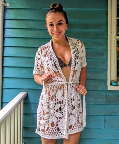 a woman in a white crochet cover up standing on the front porch of a blue house