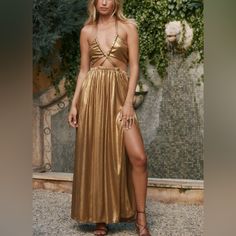 a woman in a gold dress standing next to a wall with greenery on it