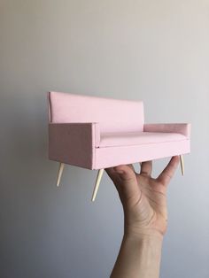 a hand holding up a pink couch with wooden legs and nails sticking out of it