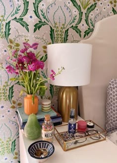 a white table topped with a lamp next to a vase filled with flowers and other items