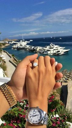 two people holding hands with boats in the water behind them and palm trees on either side