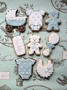 baby shower cookies are arranged on a blue and white tablecloth with teddy bears, crib, diaper, bib, bottle