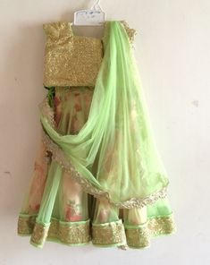 An absolutely fabulous floral lehenga from Bubblinga. The lehenga has a trendy sequin blouse with matching green piping at the neck and sleeves. The blouse is completely lined in cotton and piping at the hem , sleeve and neck prevents the sequin from coming in contact with skin. The skirt is a gorgeous twirly affair with a floral fabric with a tulle overlay in peach. The tulle is cut into kalis to get maximum flare. There are gold borders at the hem and waistline. The skirt has ties at the waist for the perfect fit and the skirt is also lined in cotton for additional body and comfort. Dress is custom made. Once you order I'll send you a measurements sheet which you need to fill out with your child's measurements. Alternately, you could just choose an age group in which case I would use the Spring Anarkali Set With Gota Work, Designer Pista Green Choli With Sequins, Pista Green Sequined Choli For Designer Wear, Designer Pista Green Sequined Choli, Spring Festive Sharara With Gota Work, Green Traditional Drape Dress For Spring, Pista Green Sequin Sets For Reception, Green Spring Dress With Traditional Drape, Pista Green Floor-length Sequin Set