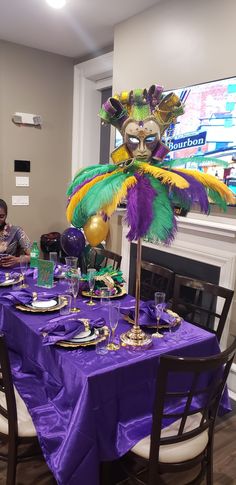 a table set with purple and green plates, silverware and a mask on it